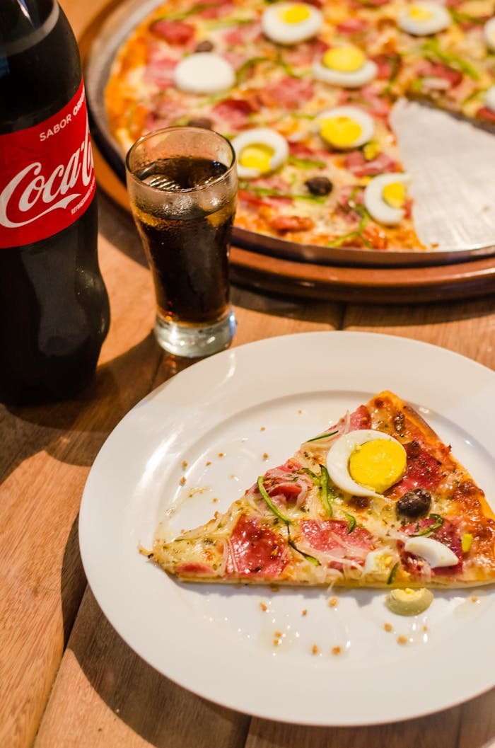 about-02 Delicious pizza with eggs and olives, paired with a refreshing cola drink. Perfect for dine-in or casual dining.