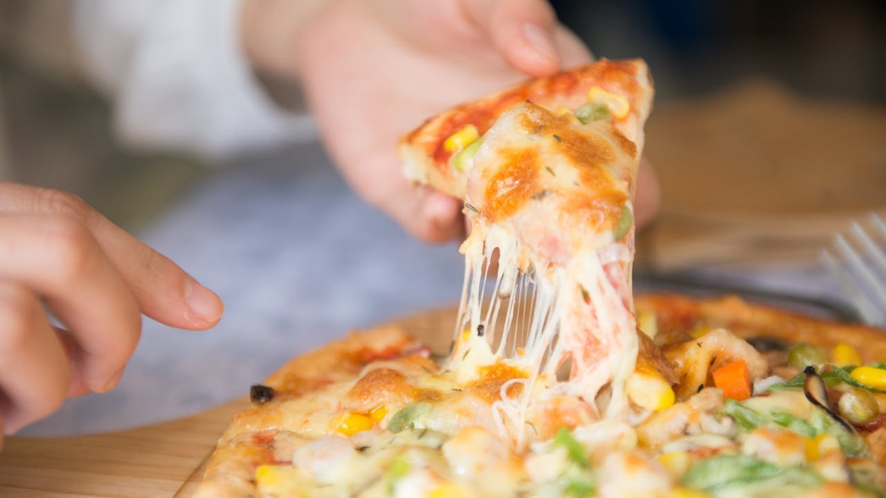 menu-01 Appetizing close-up of a cheesy pizza slice with toppings, being pulled from a freshly baked pie.
