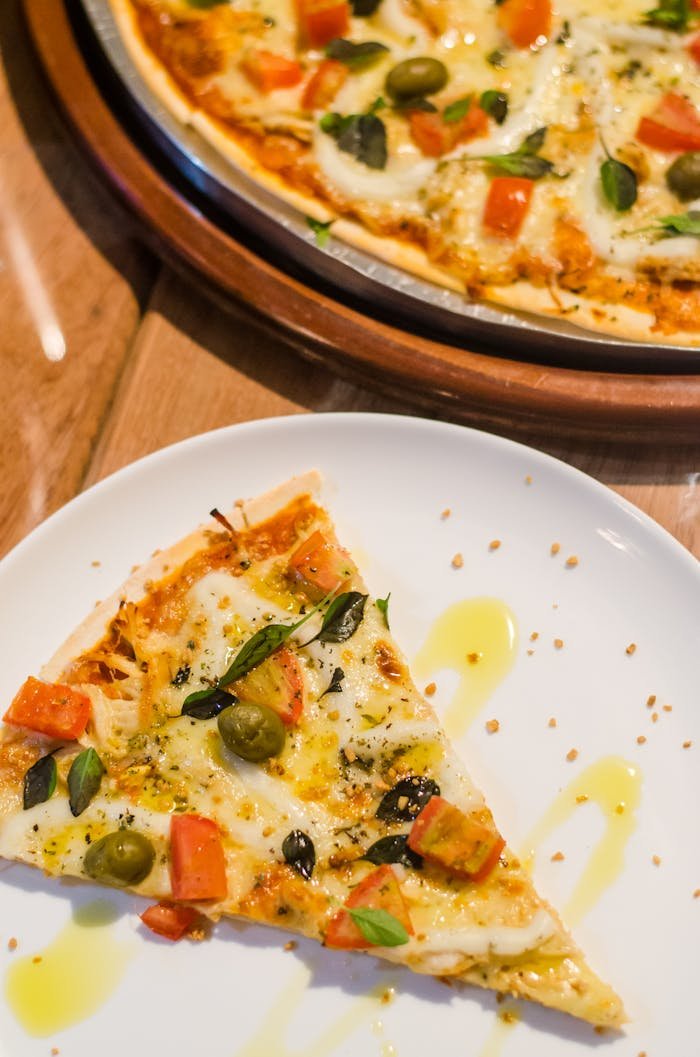 menu-03 Close-up of a delicious pizza slice with toppings like cheese, olives, and tomatoes on a white plate.